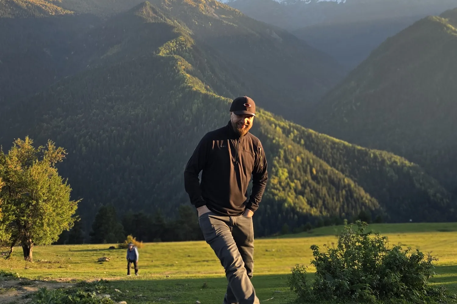 Walker on a meadow path above a forested valley in Upper Svaneti, Georgia, in late afternoon light