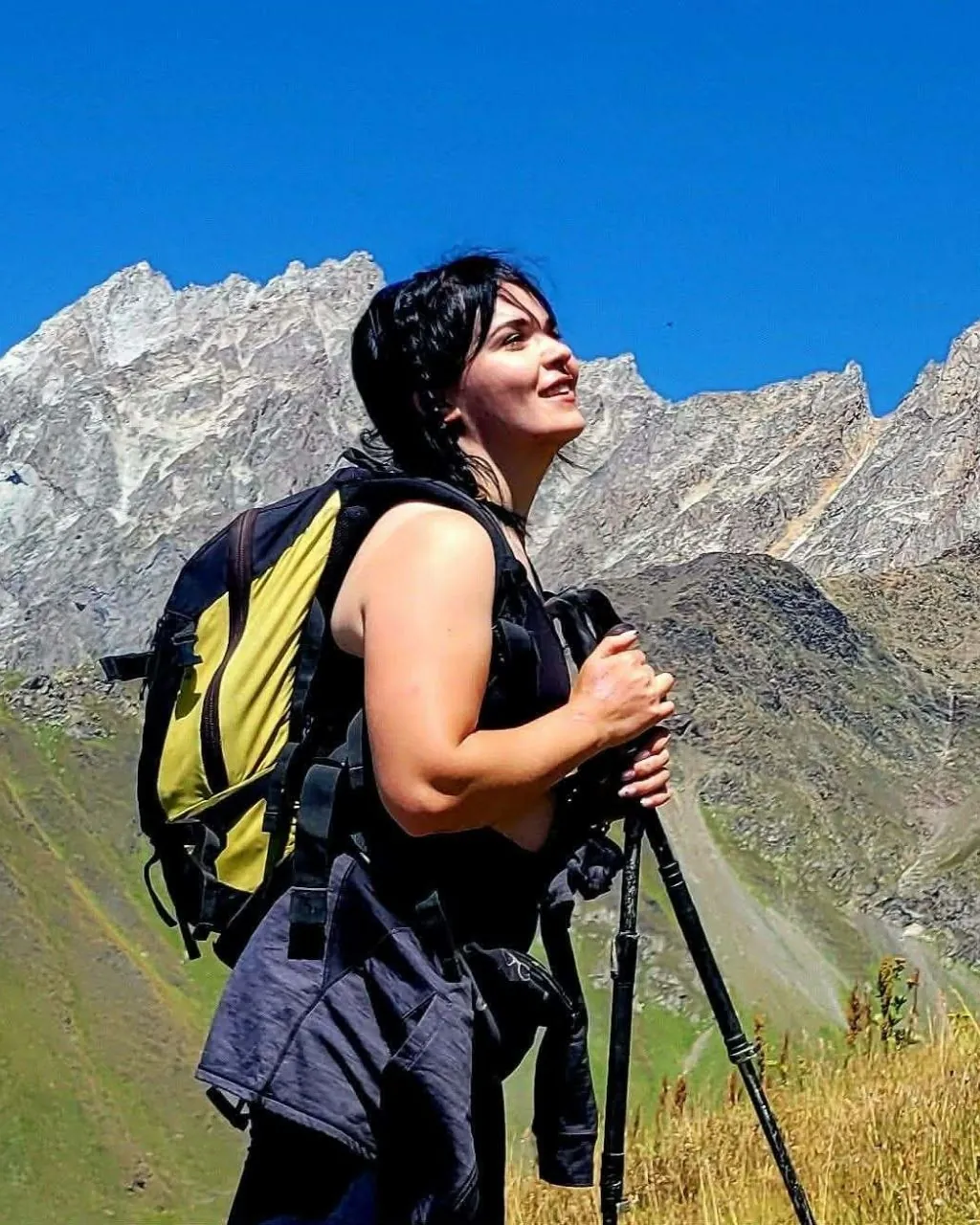 Mari, Justvia's Svaneti-born mountain guide, walking with poles below a rock face in the Caucasus, Georgia