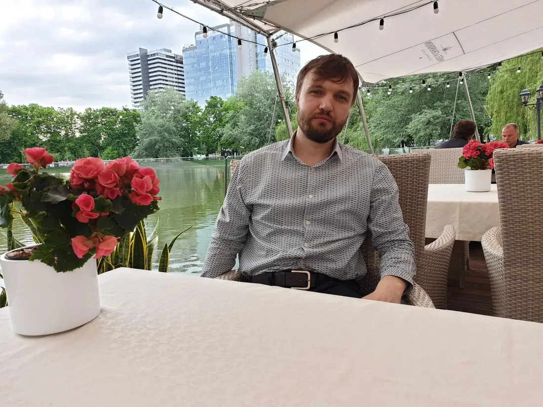 Jurijs at a riverside table in Georgia, roses on the table and the city behind