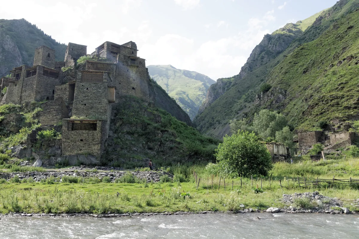 Medieval stone fortress houses and towers of Shatili above a river and meadow, Georgia