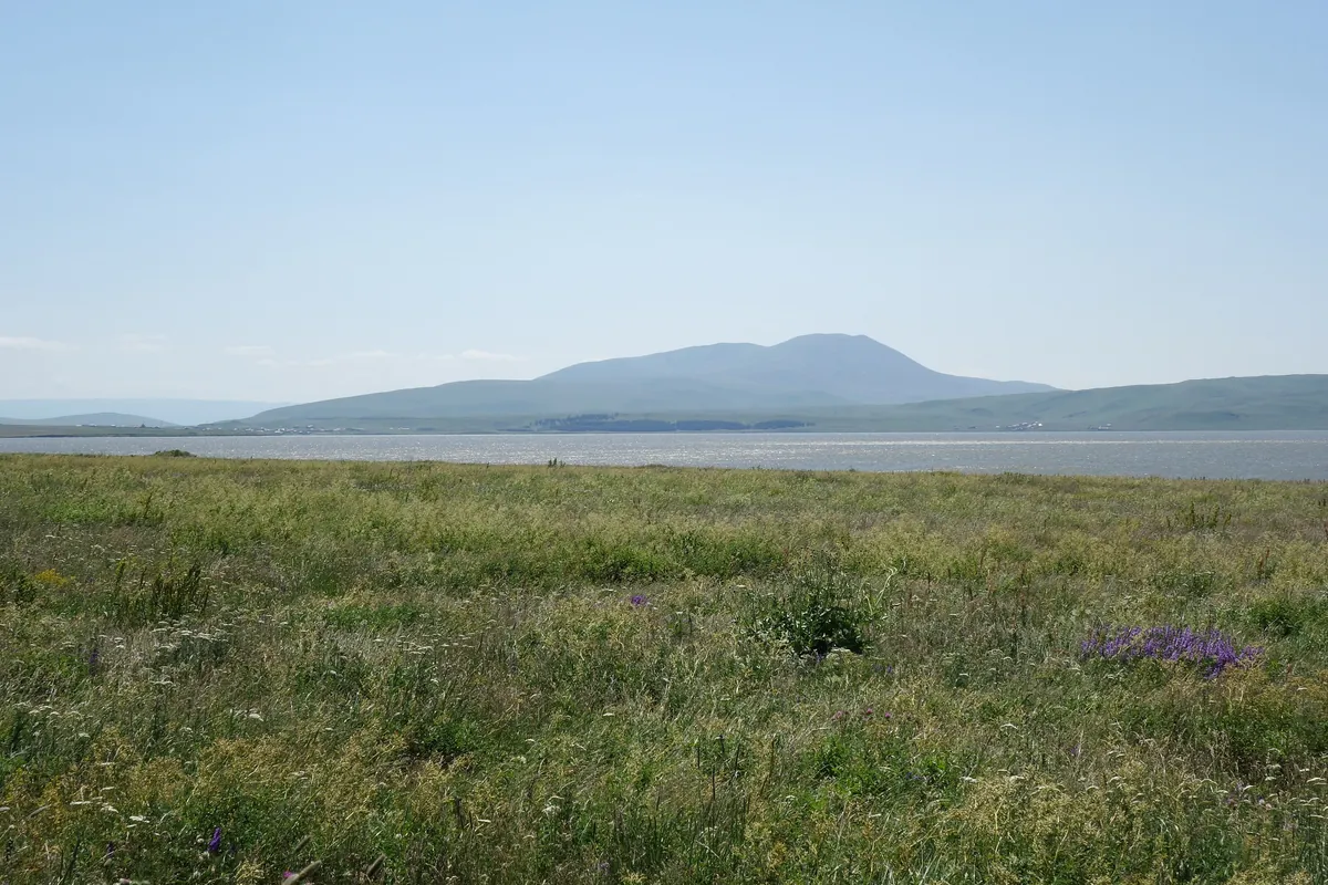 A wide grassy plateau and lake with a low mountain beyond, Javakheti, Georgia