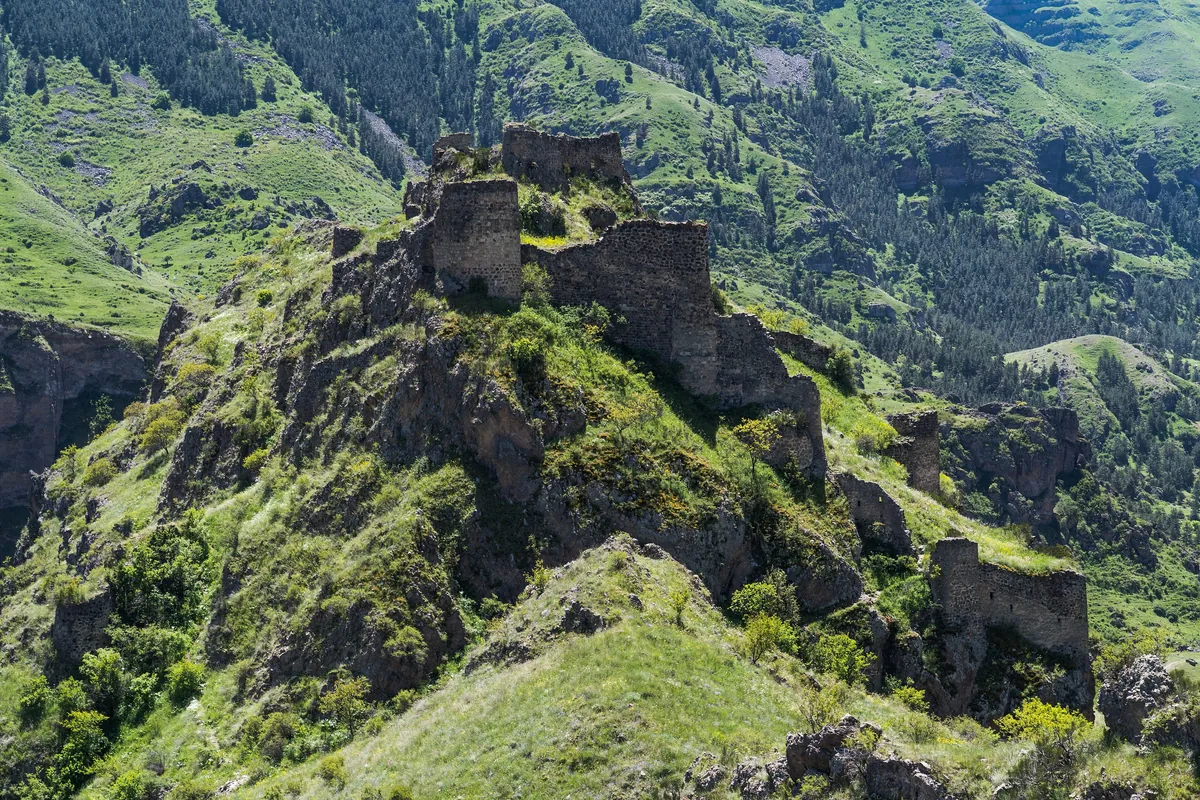 The ruined Tmogvi fortress on a green rocky hill above a valley, Georgia