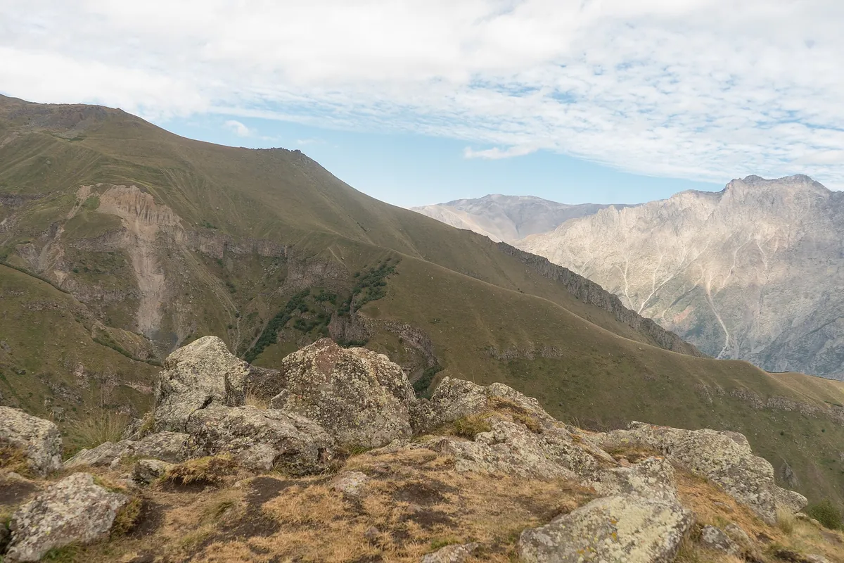 Rocks on a high ridge in Kazbegi National Park looking across a deep valley to a pale mountain range, Georgia